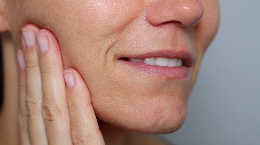 Nærbilde av en person som holder hånden mot kinnet, trolig på grunn av smerter eller hevelse i munnen