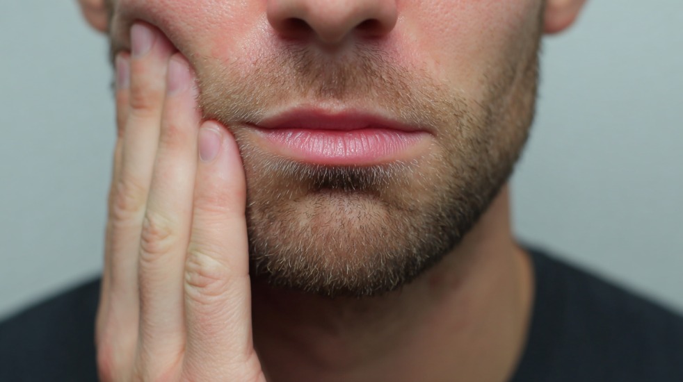 Nærbilde av en mann som holder hånden mot kinnet og ser ut til å ha vondt etter en tannskade