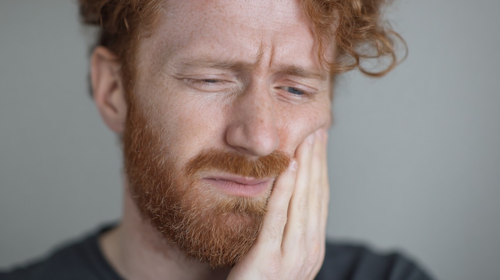En mann med rødt hår og skjegg holder hånden mot kinnet og ser ut til å ha tannverk