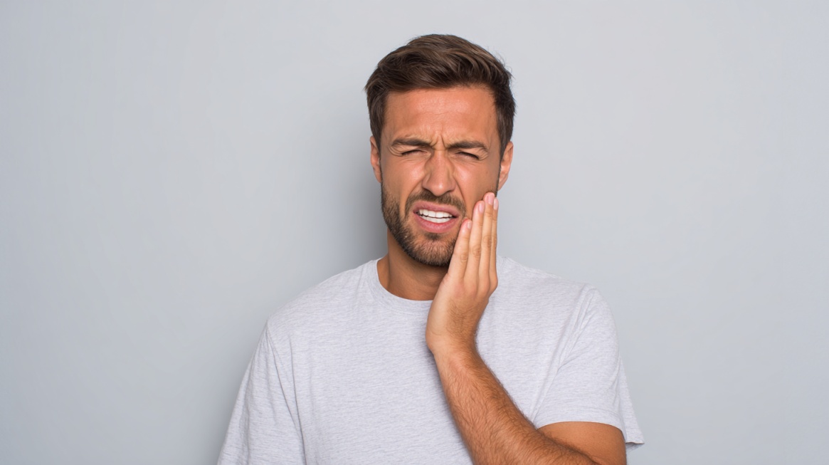 Mann holder seg på kinnet med tydelig smerteuttrykk