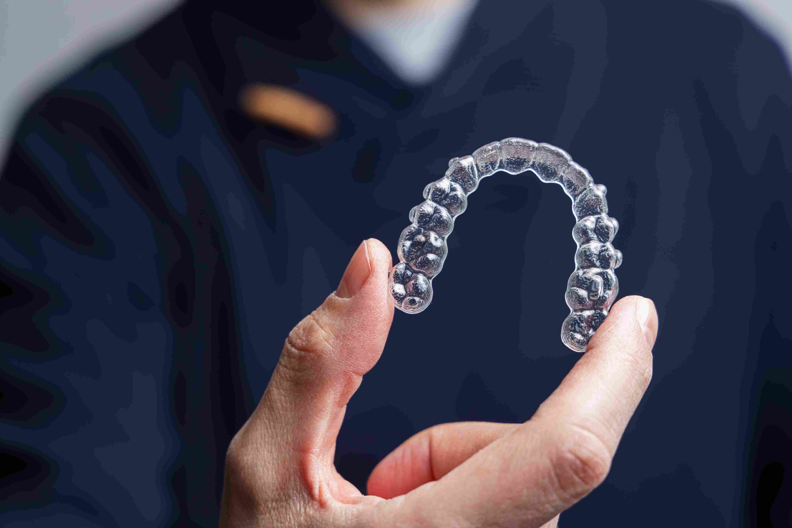 Person holder en gjennomsiktig tannreguleringsskinne (aligner) i hånden