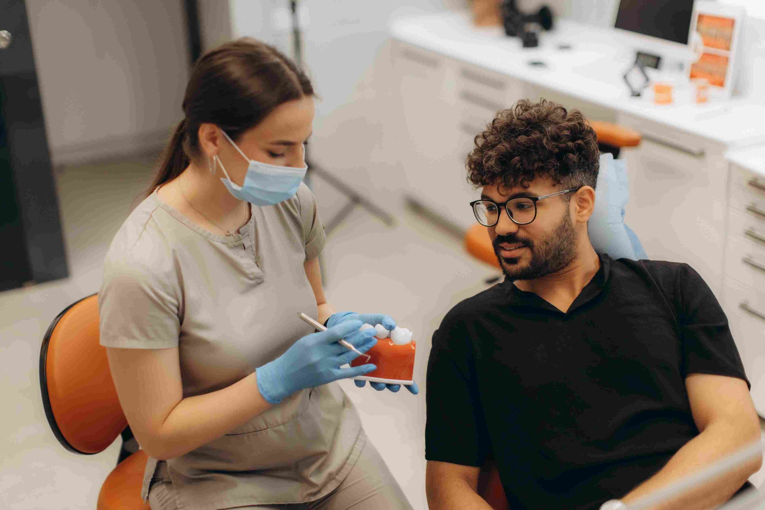 Tannlege viser en tannmodell til en pasient under en konsultasjon om tannerstatningsalternativer som implantater og broer.Tannlege viser en tannmodell til en pasient under en konsultasjon om tannerstatningsalternativer som implantater og broer.