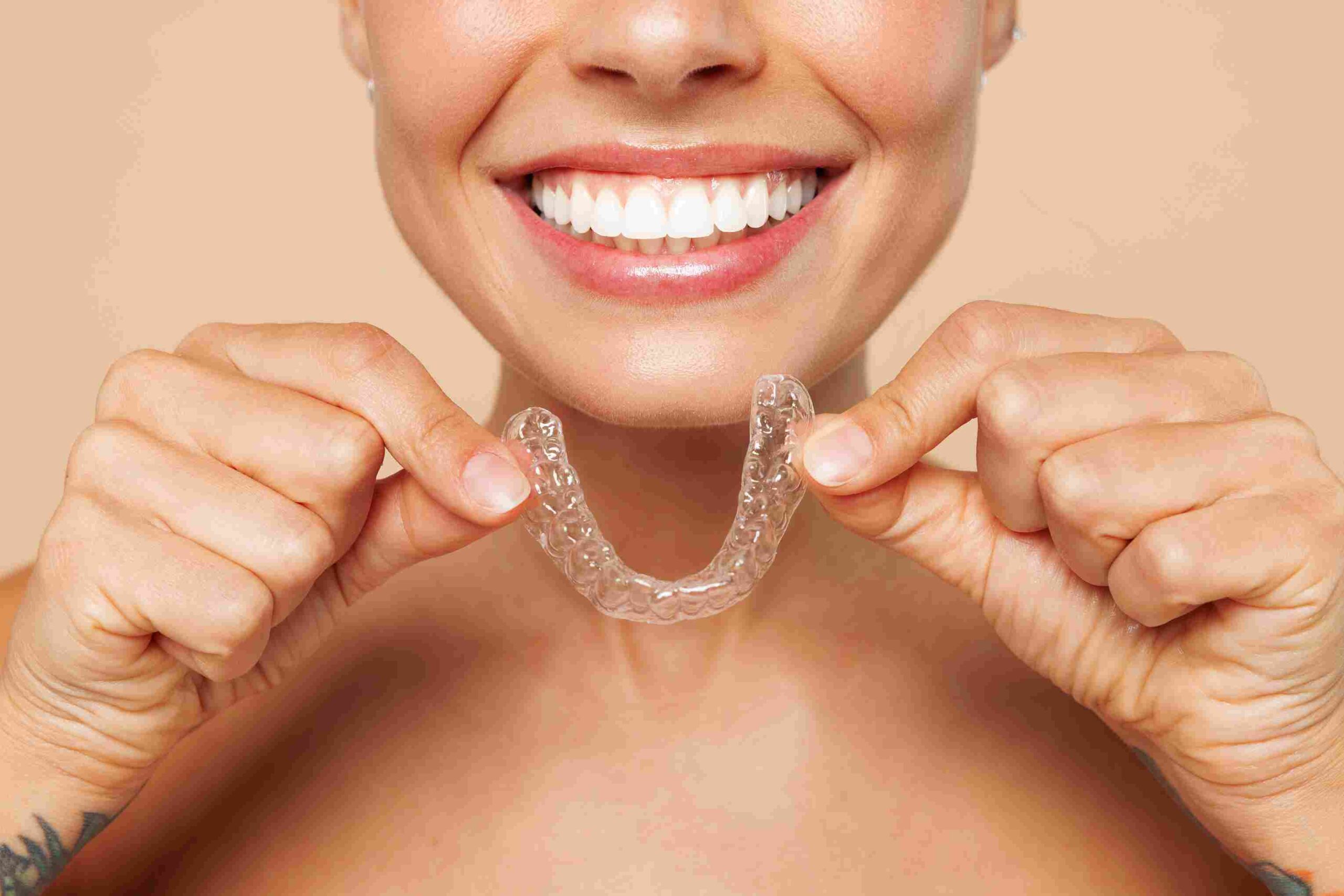 Kvinne som holder gjennomsiktige Invisalign-skinner foran et rett og hvitt smil